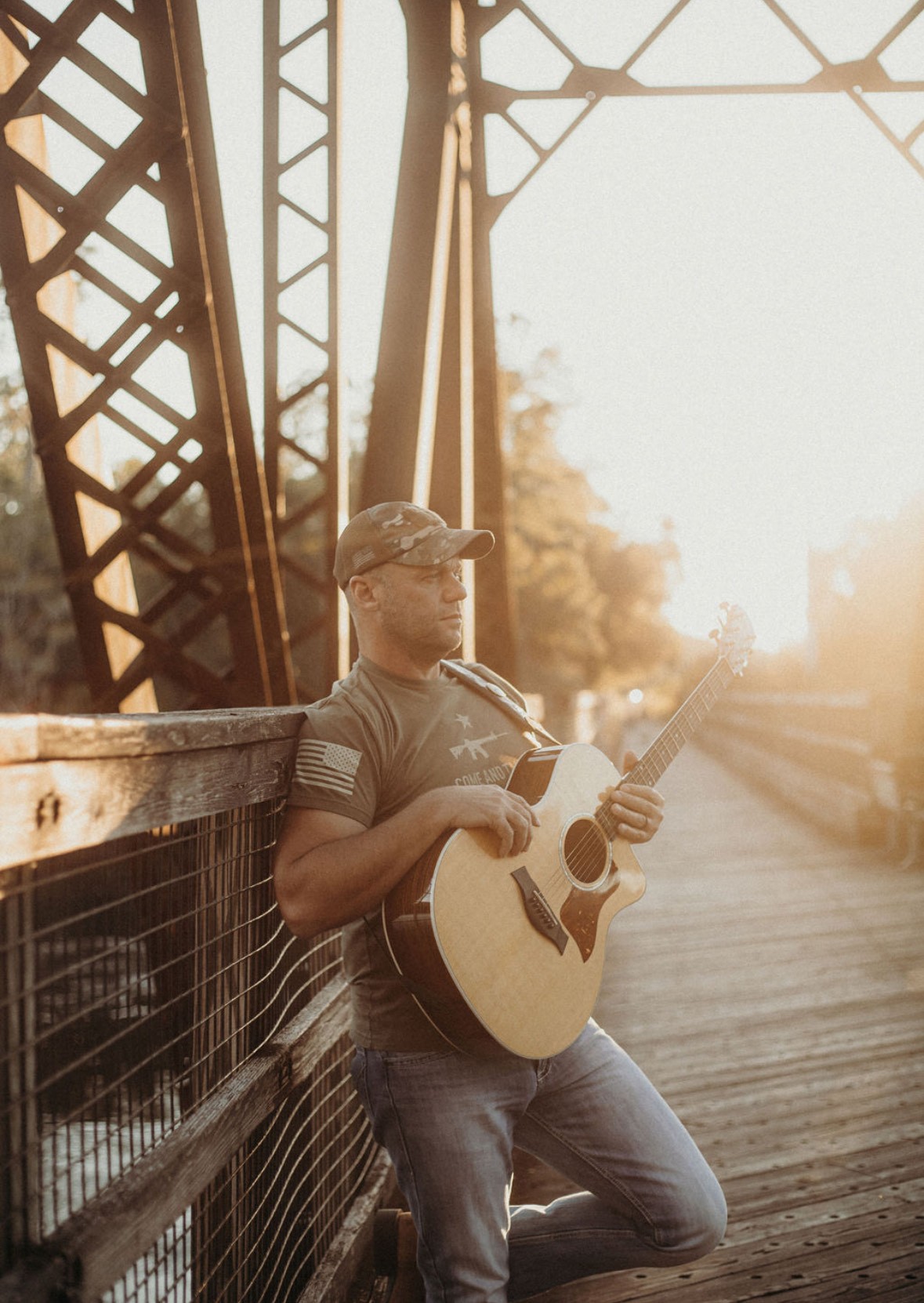 Cliff Suber holding a guitar while relaxedly standing and leaning on a trussel's guardrail.